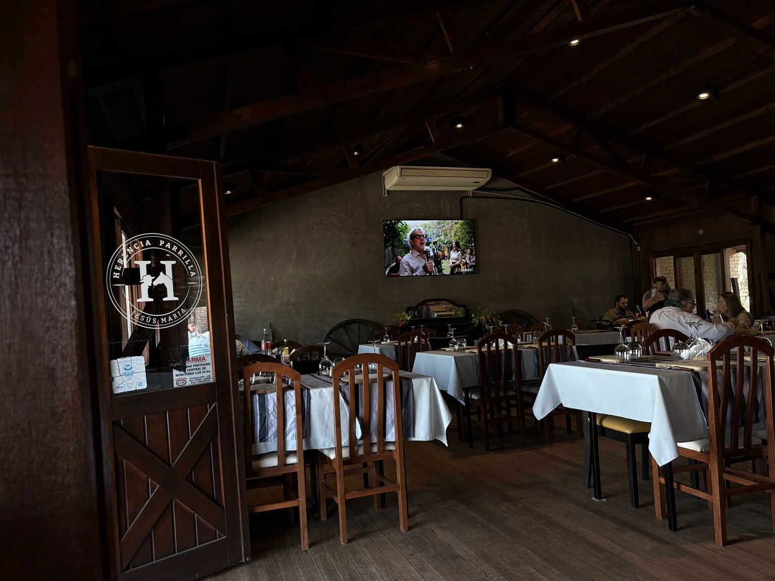Salón de Herencia Parrilla con techo de madera, mesas con manteles blancos y comensales